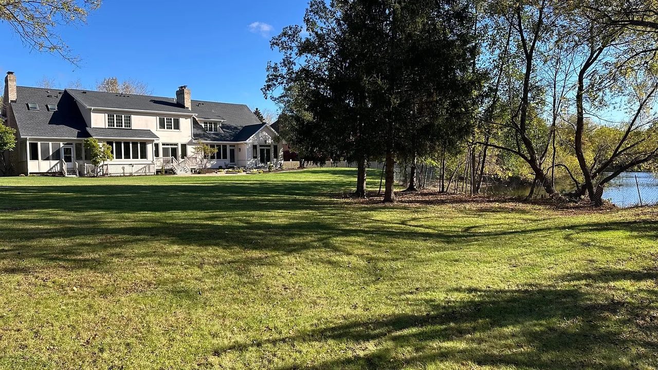 Rear of the residence with a screened porch, open lawn and water beyond the tree line.